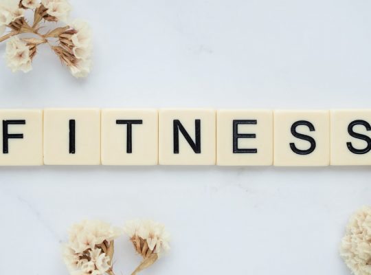 Close-up of scrabble tiles spelling 'FITNESS' on a marble surface with white flowers.