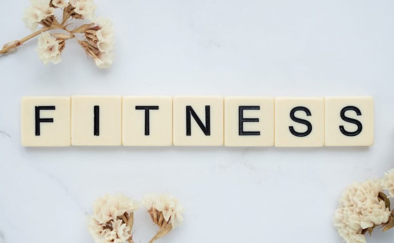 Close-up of scrabble tiles spelling 'FITNESS' on a marble surface with white flowers.
