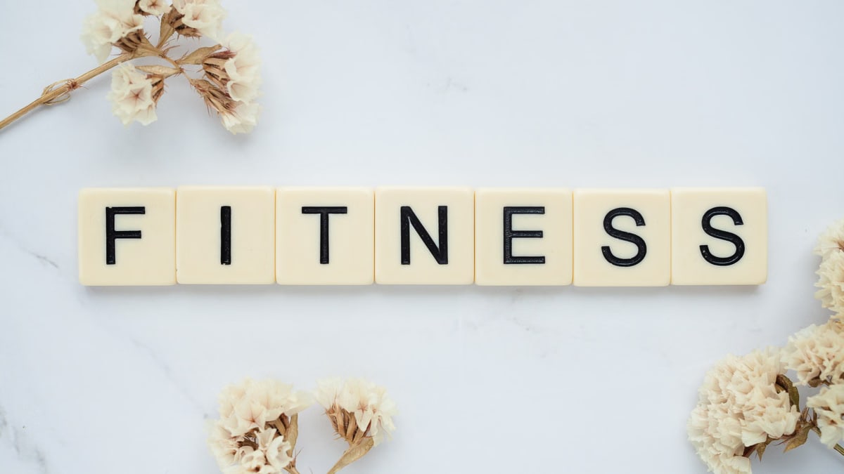 Close-up of scrabble tiles spelling 'FITNESS' on a marble surface with white flowers.